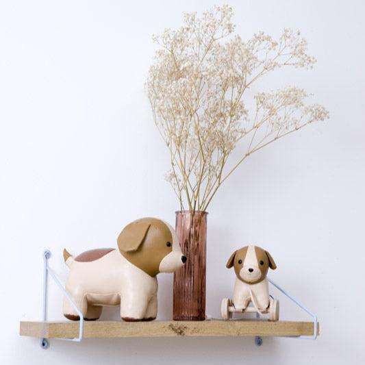 Two dog-shaped figurines on a shelf with a vase of dried flowers against a white background