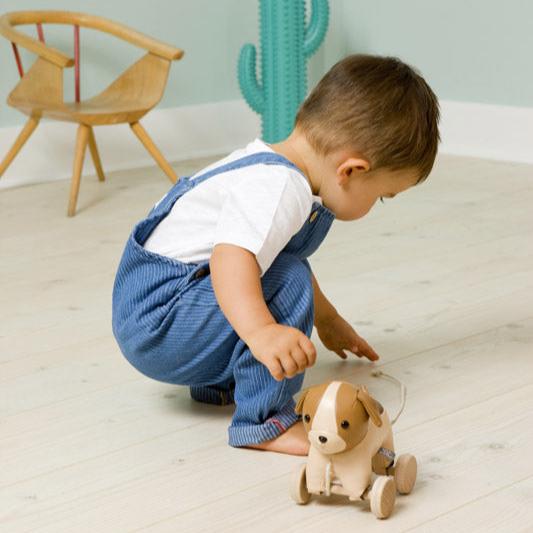 Child playing with a wooden toy dog on a light wood floor.