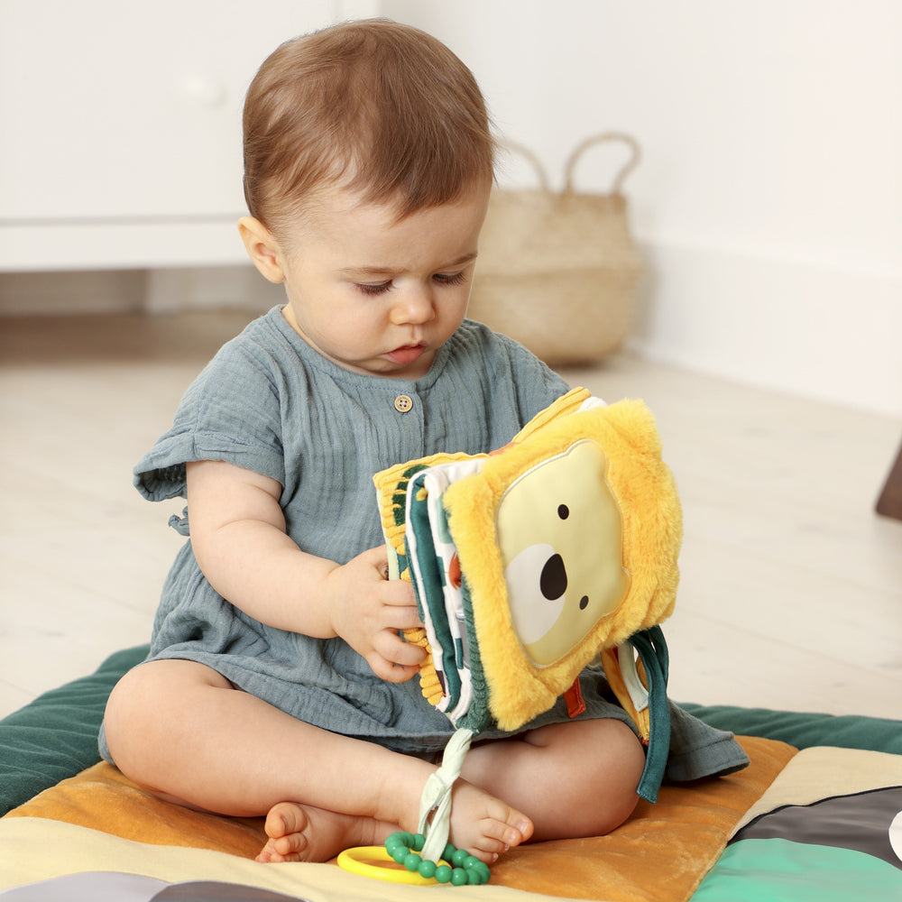 Child playing with a soft toy lion on a wooden floor.