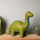 Green dinosaur-shaped object on a wooden surface with a neutral background