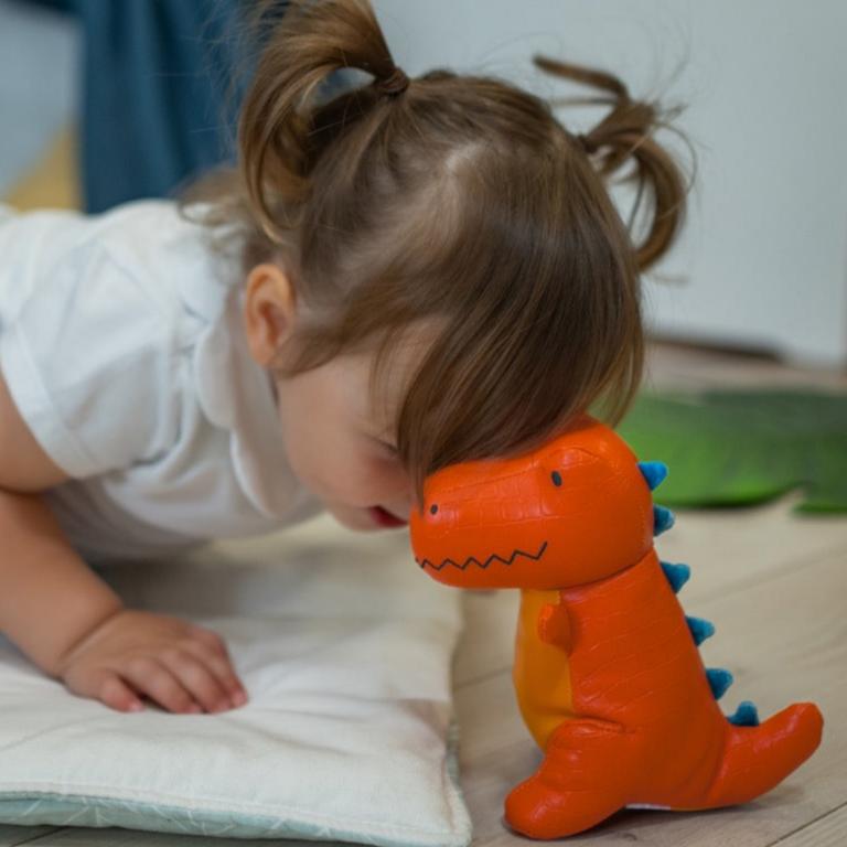 Child playing with an orange dinosaur toy on a wooden floor.