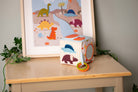 Children's toy block with animal designs on a wooden surface next to a framed picture of dinosaurs.