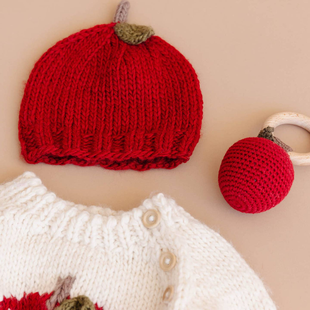 Knitted red apple hat and ball on a beige background