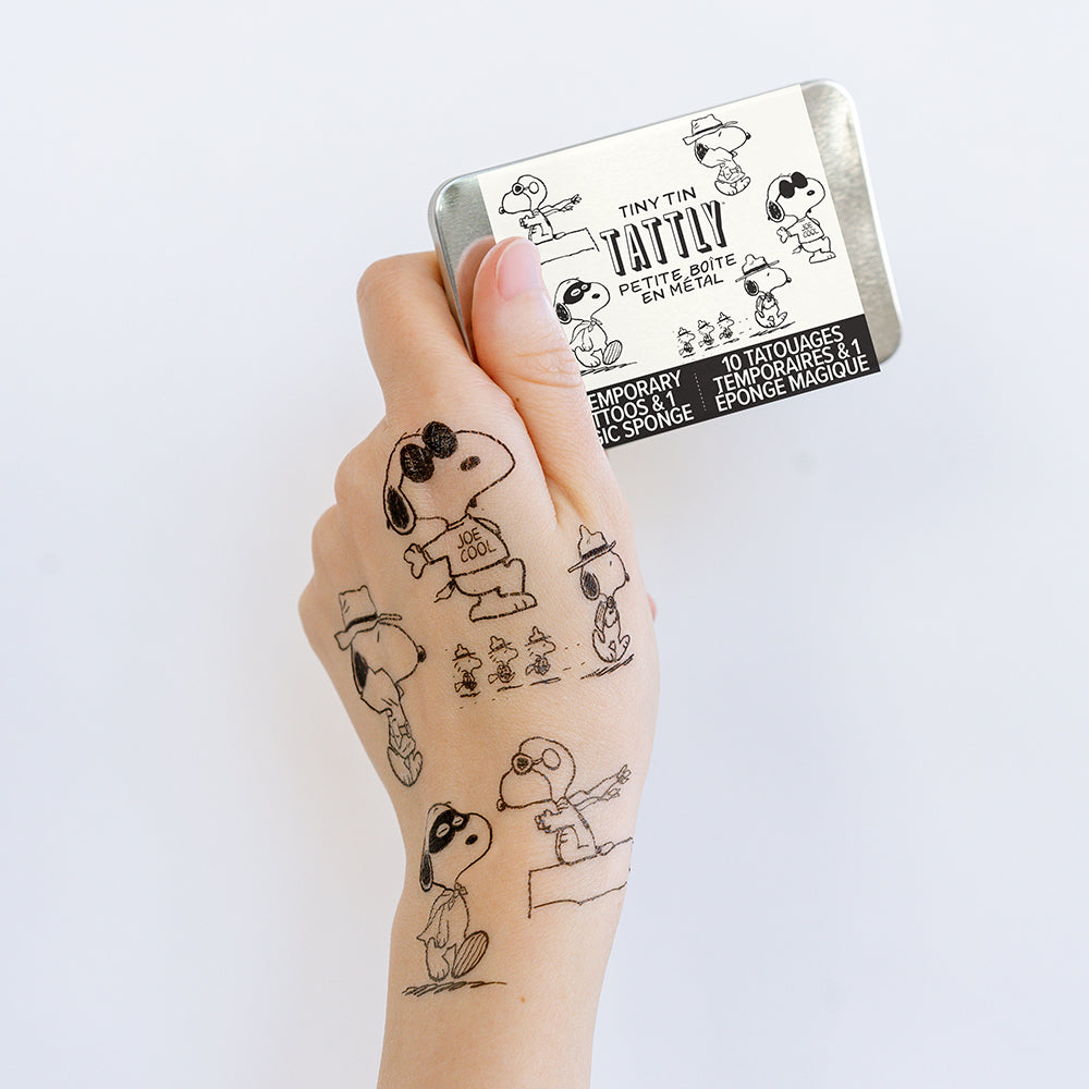 Hand with temporary tattoos of cartoon characters and a tin labeled 'Tiny Tin Tattoo' on a white background.