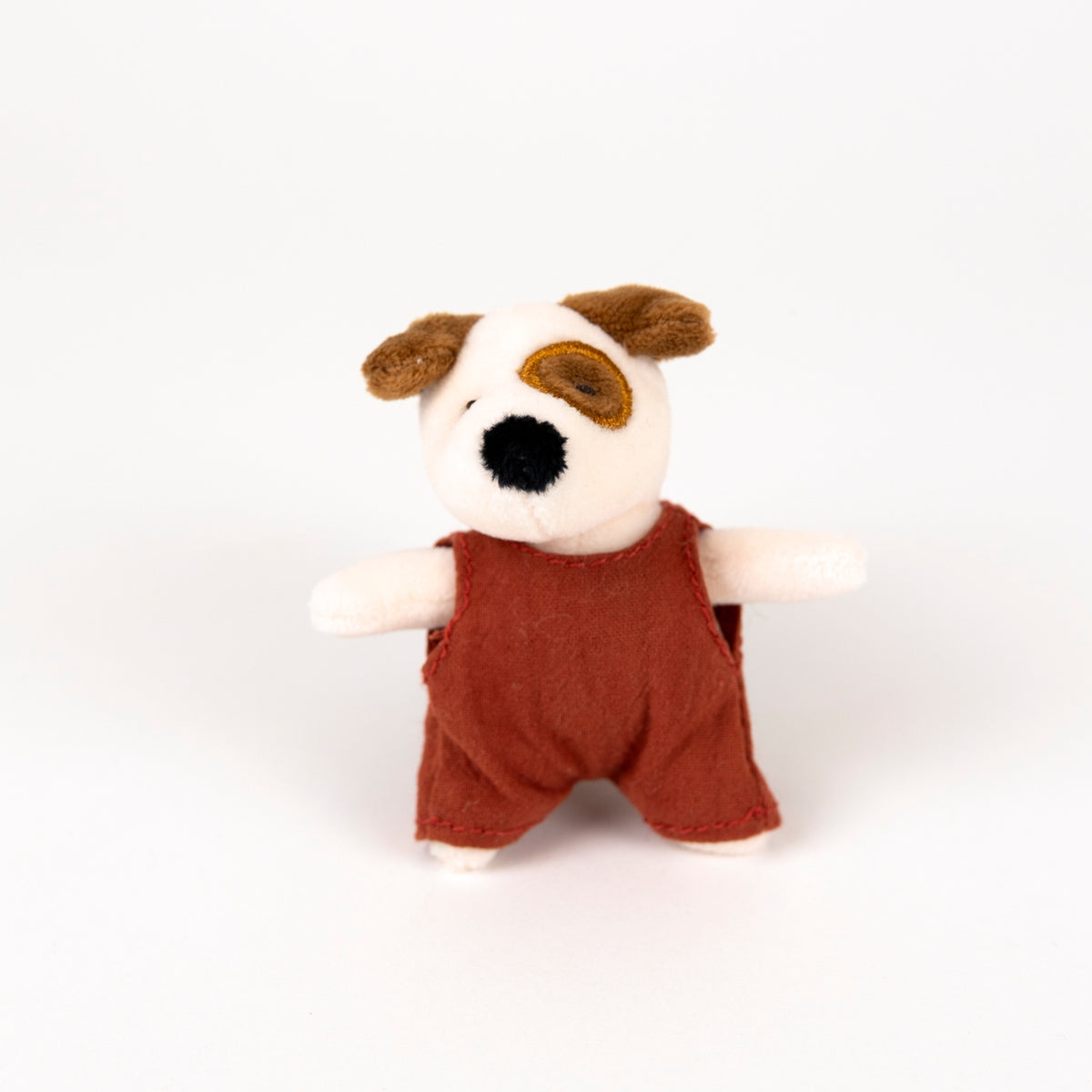 A small plush dog toy with a white face, brown ears and eye patch, black nose, and a rust-red romper photographed on a clean white background.