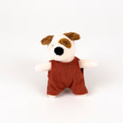 A small plush dog toy with a white face, brown ears and eye patch, black nose, and a rust-red romper photographed on a clean white background.