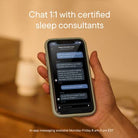 Hand holding a smartphone with a sleep consultation app open, set against a warm indoor background.