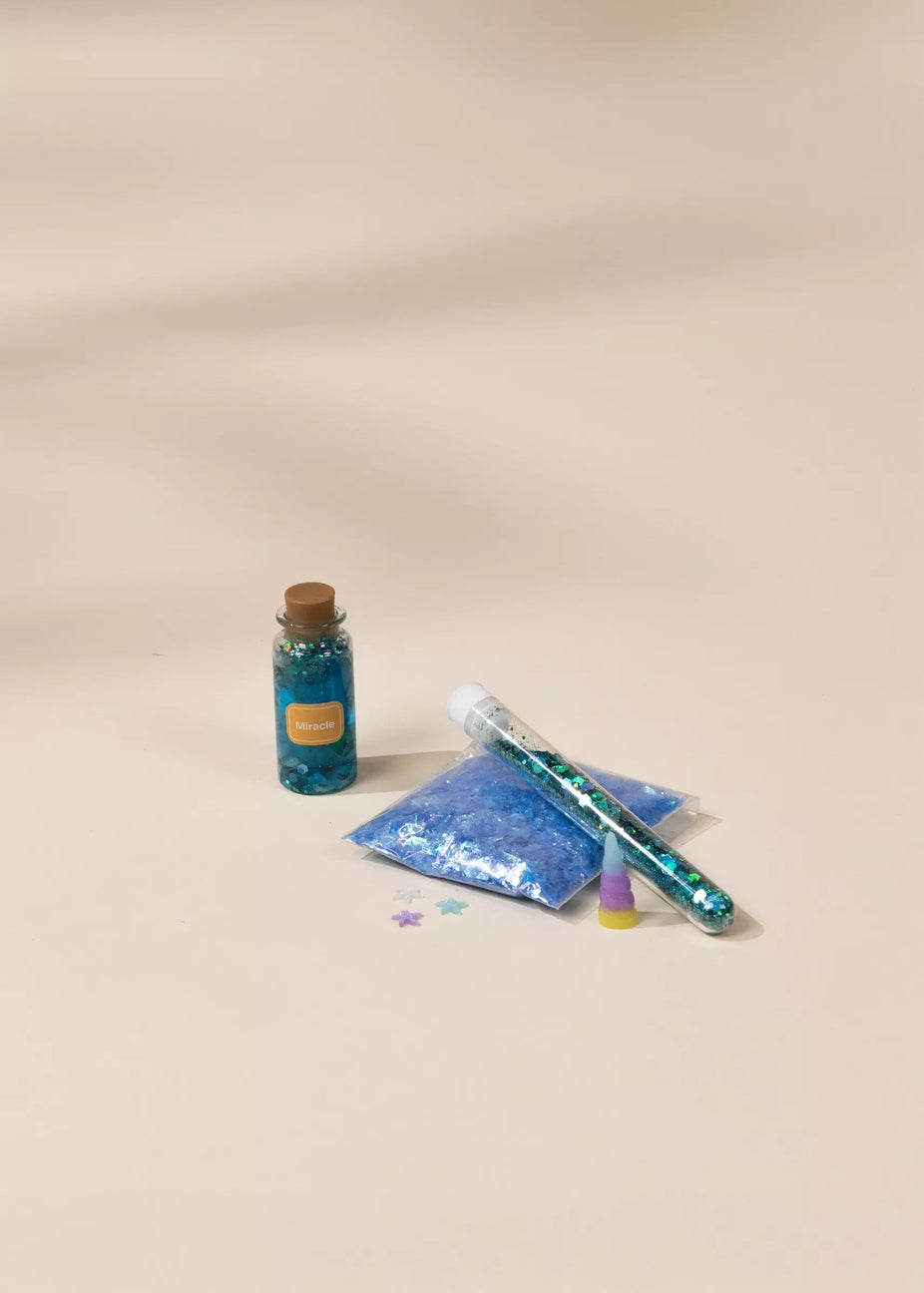 Blue glittery bottle, bag, and tube on a beige background