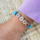Wooden bracelet with letter beads on a wrist against a woven mat background