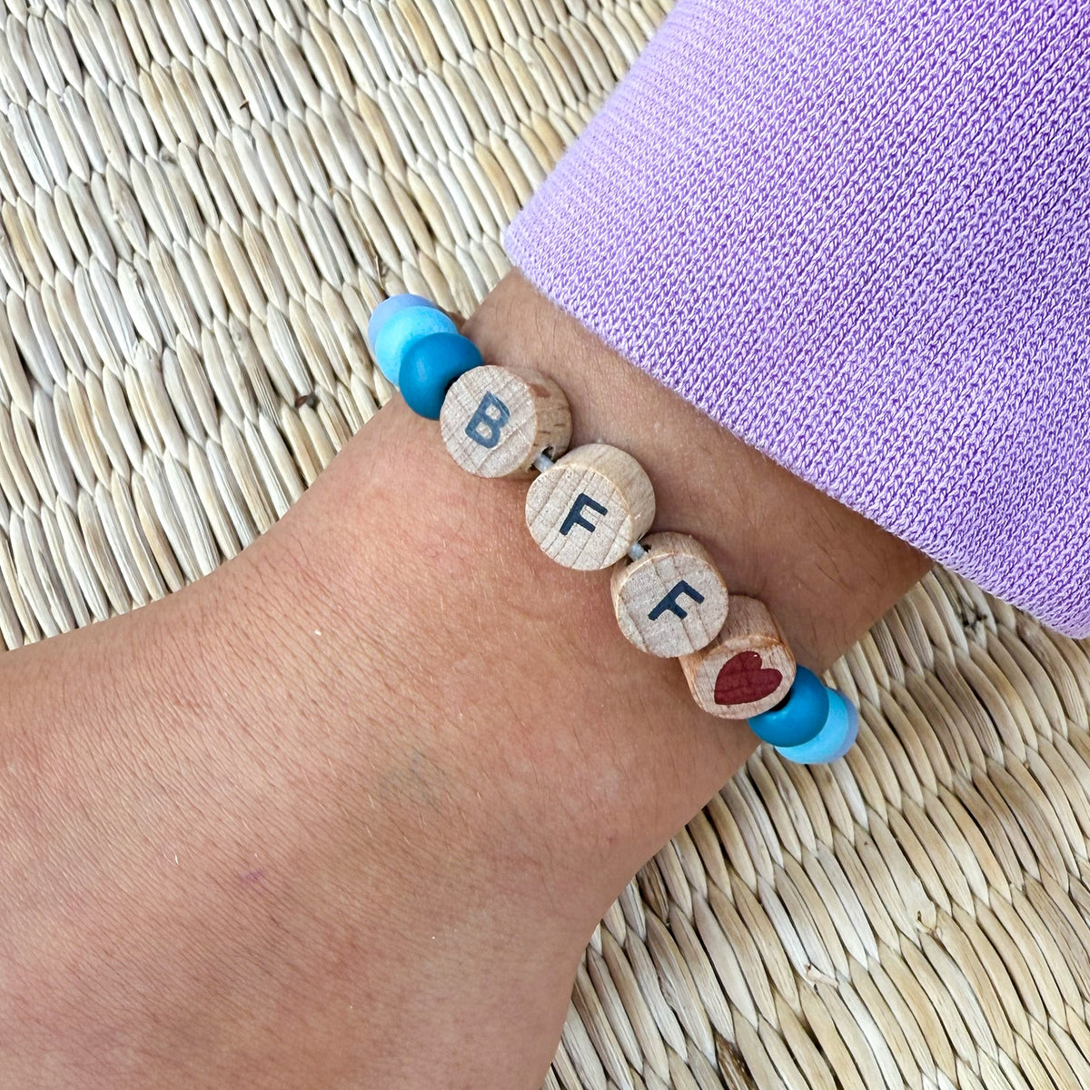 Wooden bracelet with letter beads on a wrist against a woven mat background
