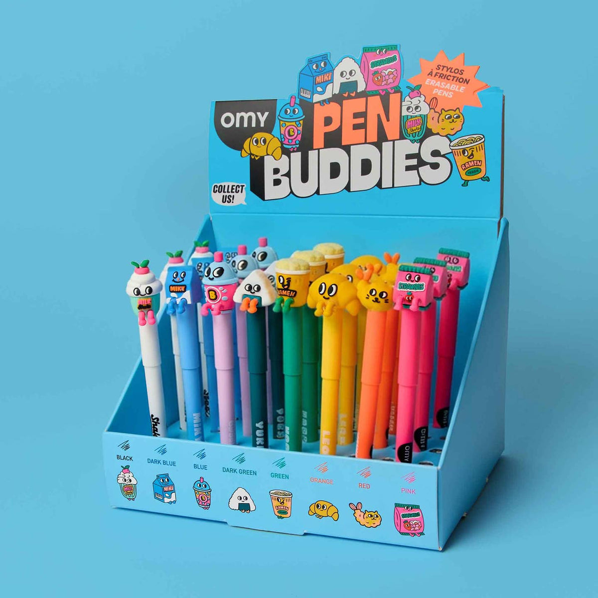 A blue Omy Pen Buddies collectible display box filled with colorful cartoon pen toppers and matching pens, photographed on a solid light blue background.