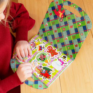 Child playing with a colorful Christmas-themed activity board on a wooden floor.