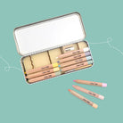 Set of makeup pencils in a tin with visible brand name on a teal background