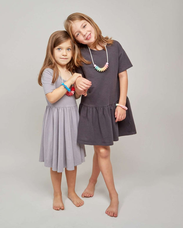 Two young girls wearing gray dresses standing against a plain background