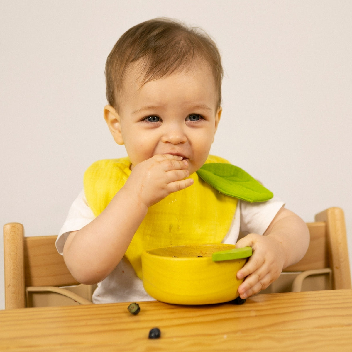Baby wearing a yellow bib sitting at a table with a green leaf