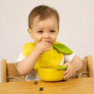 Baby wearing a yellow bib sitting at a table with a green leaf
