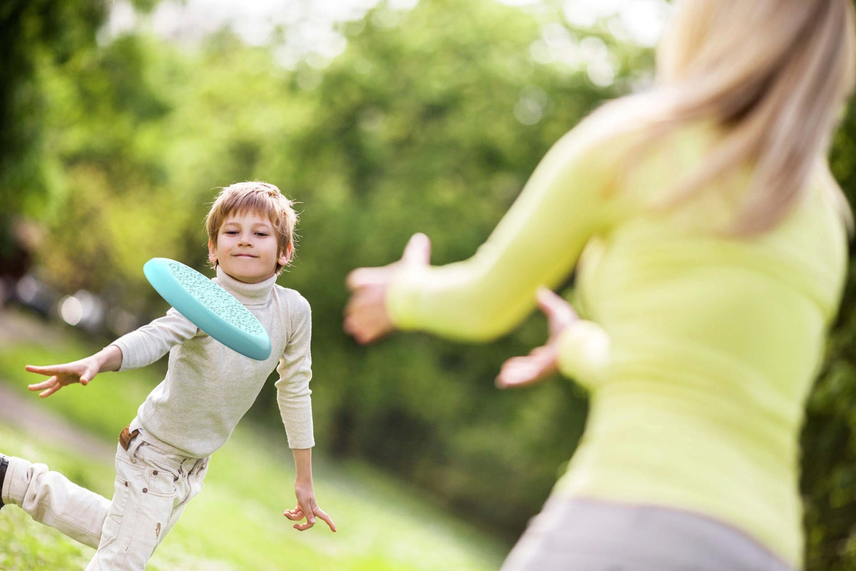 A child playing catch with a flying disc outdoors, throwing it toward an adult standing nearby.
