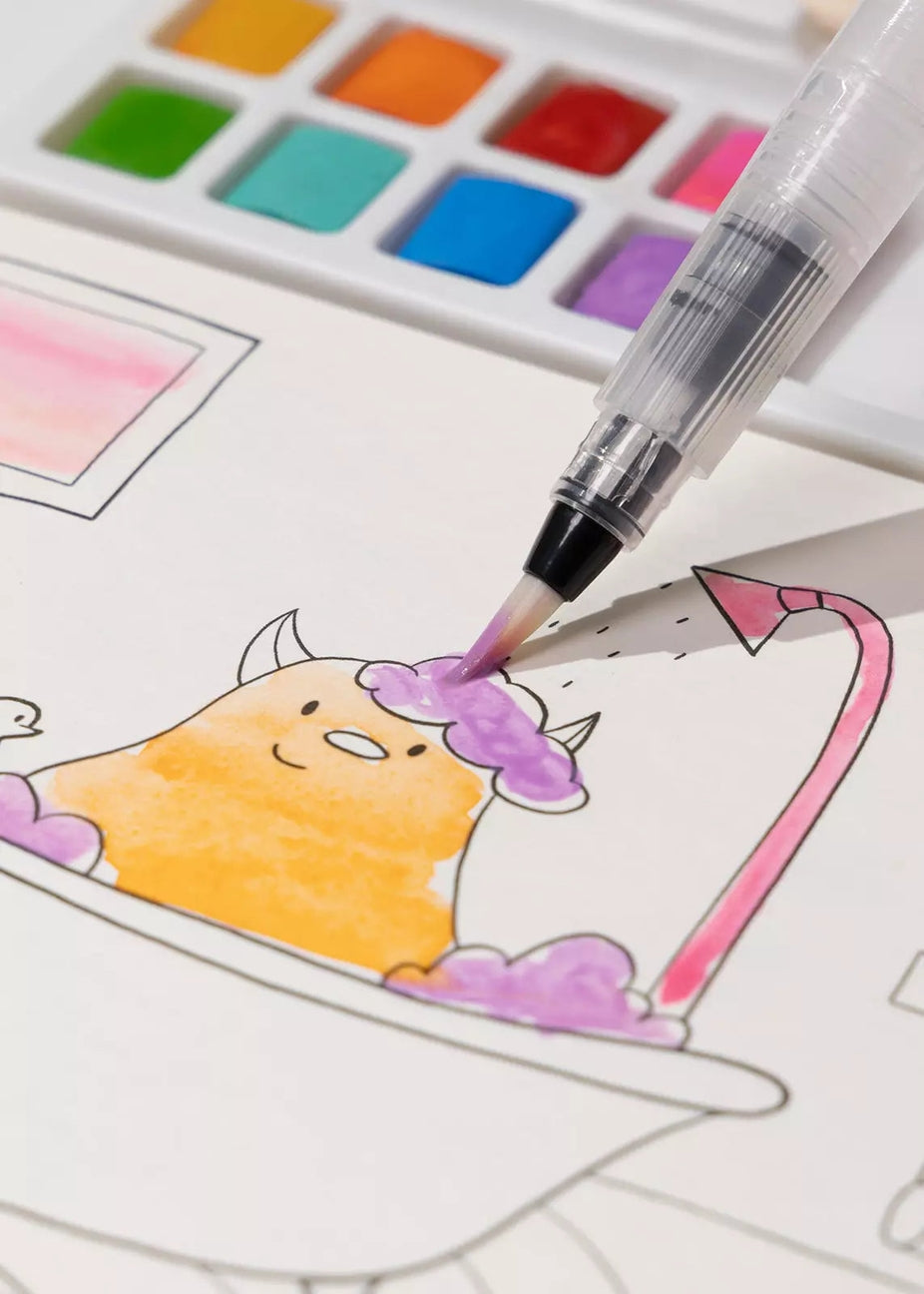 A close-up of a watercolor brush pen being used to color a cartoon character in a bathtub, with a watercolor palette visible in the background.