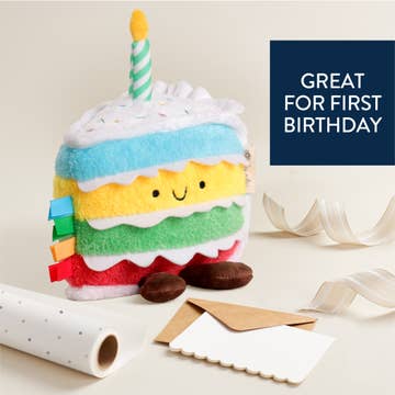 Colorful plush toy resembling a birthday cake with a candle on a light background.