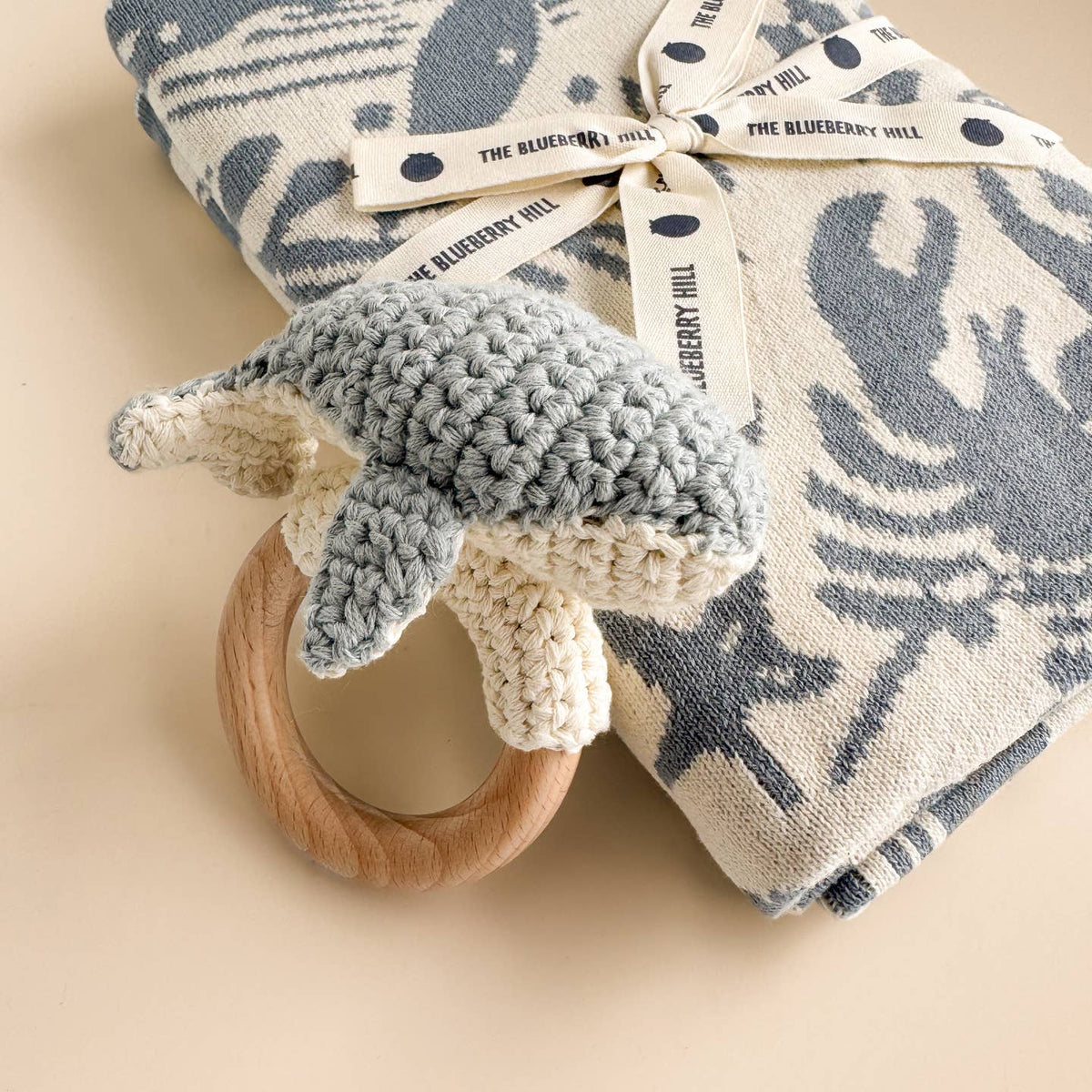 Baby teething ring with knitted gray cover and patterned blanket on beige background