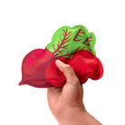 Hand holding a red radish-shaped object with green leaves on a white background