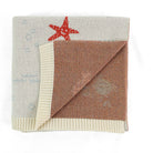A folded knit blanket with a warm brown center, cream ribbed borders, a red starfish motif, and faint blue nautical patterns on a white background.