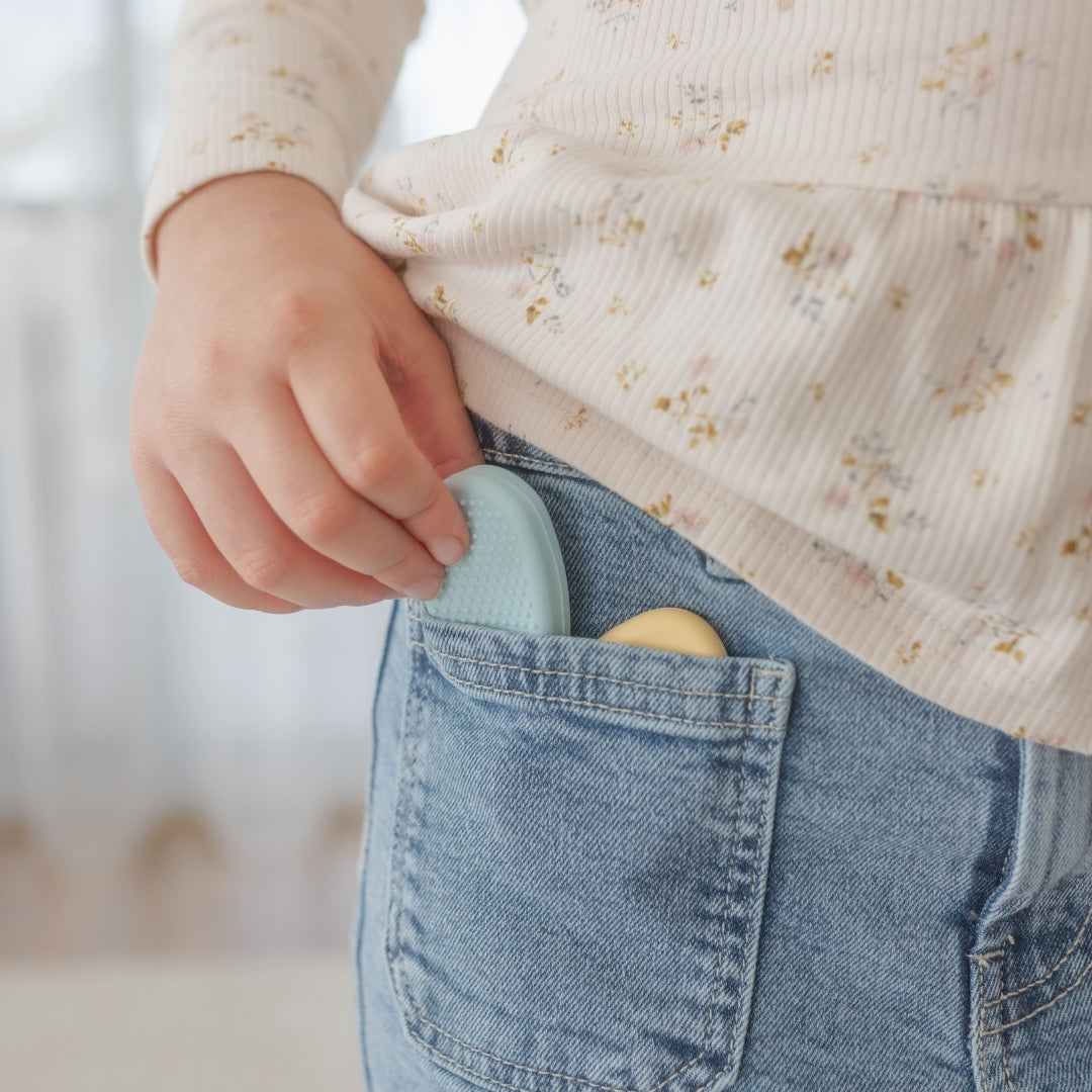 Person wearing a floral shirt and blue jeans with a light blue object in the pocket.