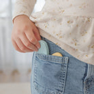 Person wearing a floral shirt and blue jeans with a light blue object in the pocket.