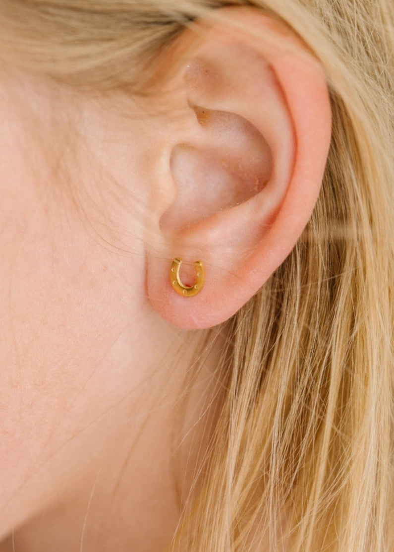 Close-up of an ear wearing a gold hoop earring with blonde hair.