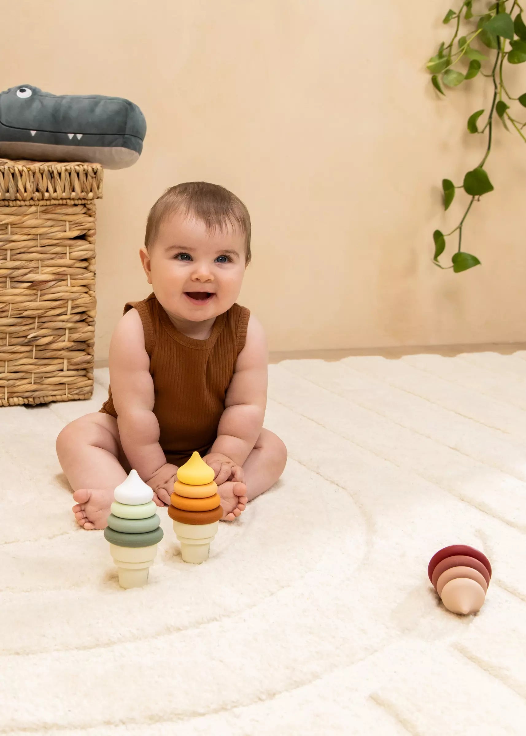 Baby sitting on a white blanket with colorful wooden toys, smiling.