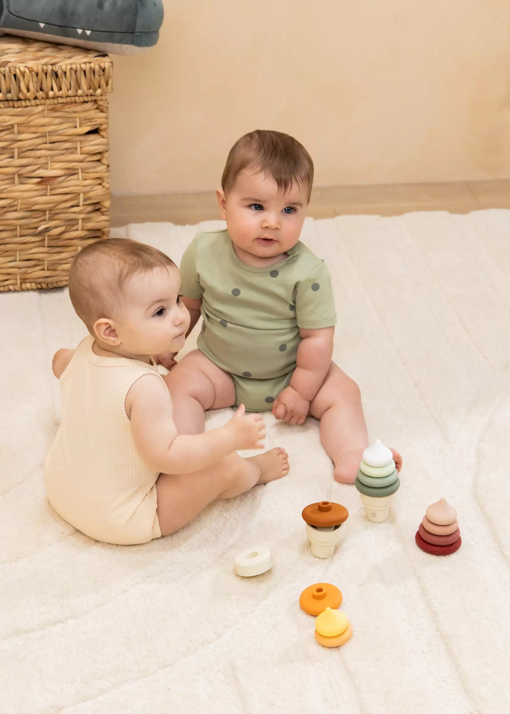 Two babies playing with wooden toys on a bed