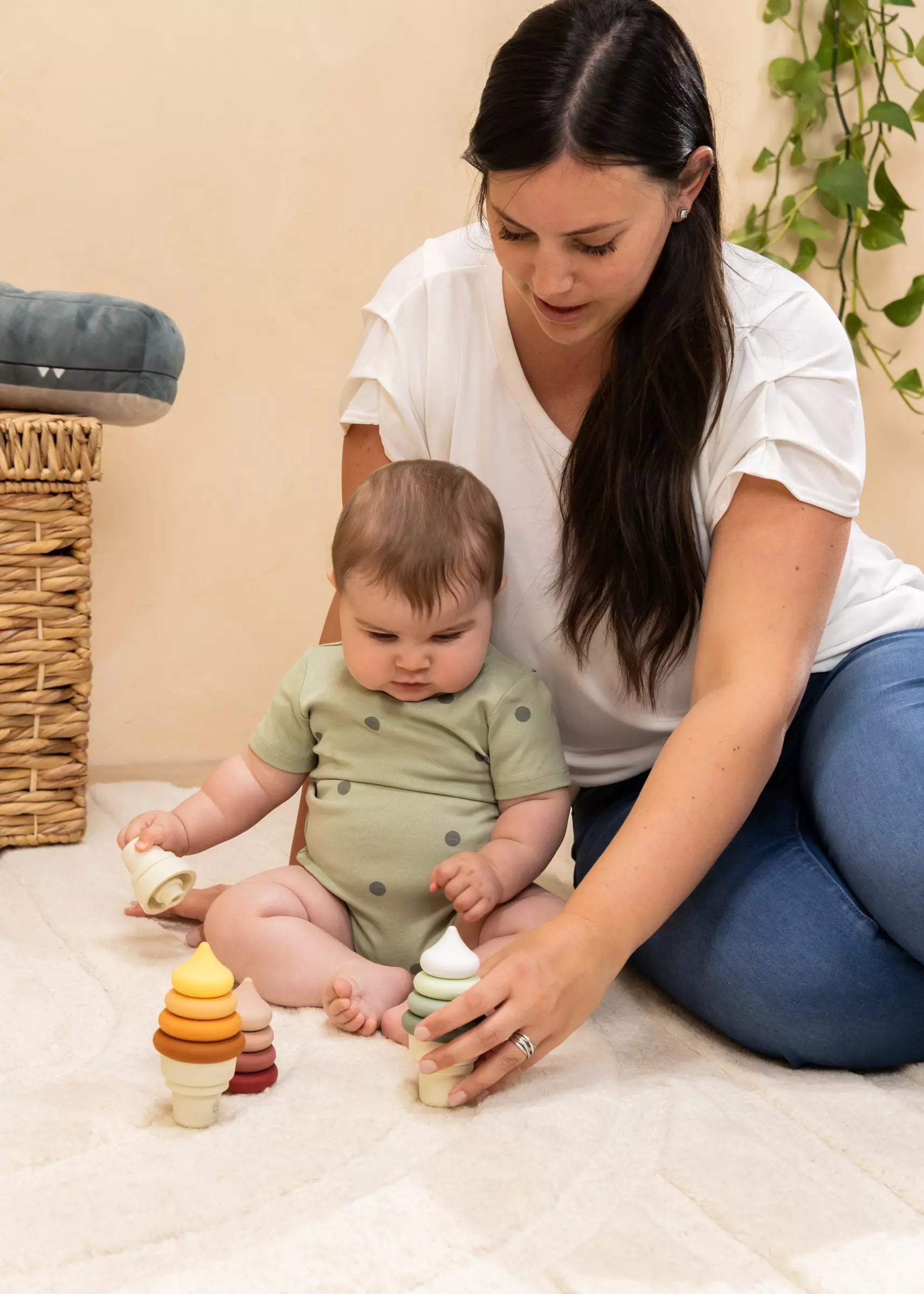 Woman and baby playing with colorful wooden toys on a light-colored floor.