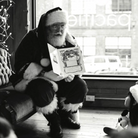 Black and white photo of a person in a Santa Claus costume holding a book, sitting on a couch.