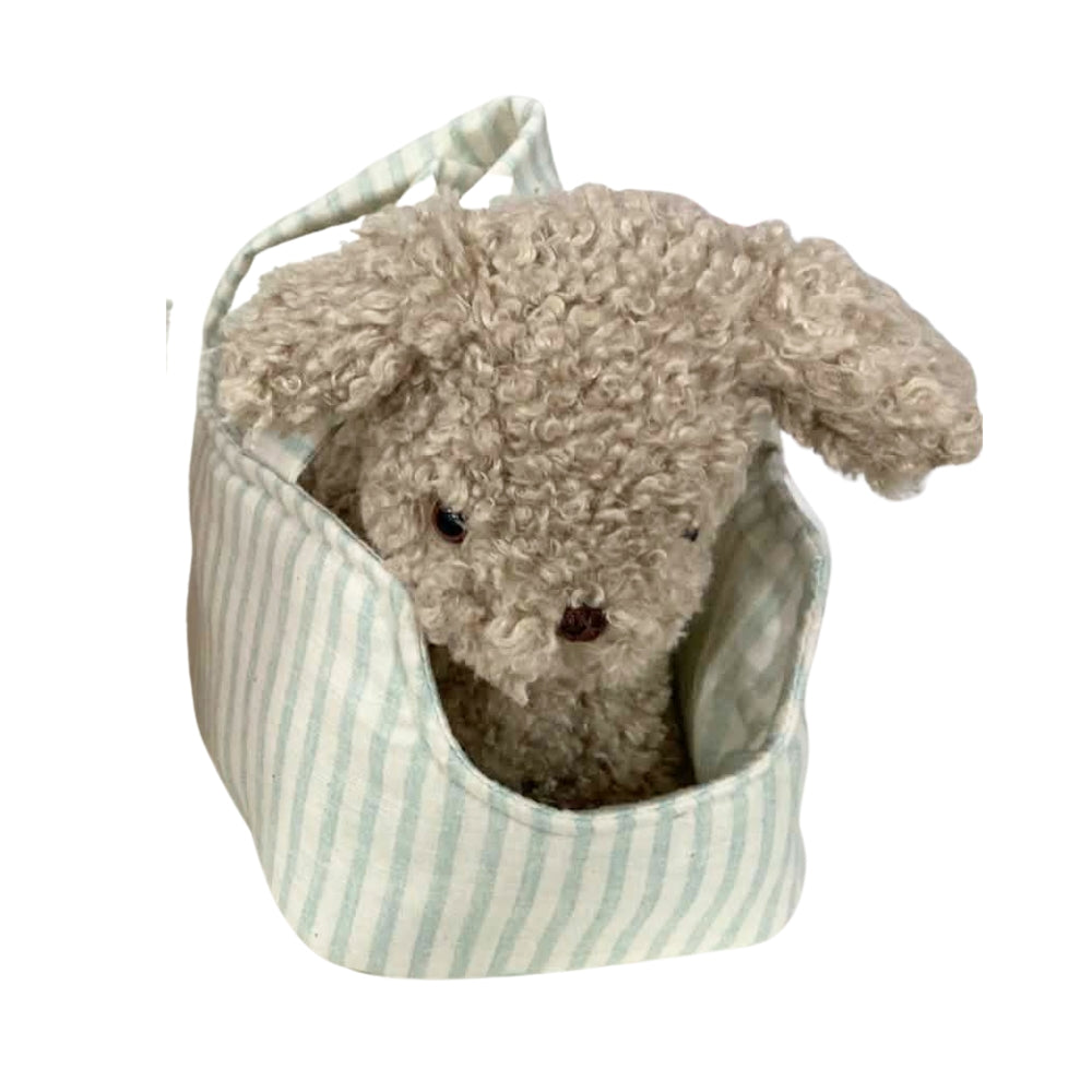 A small beige curly-haired plush toy dog sitting inside a soft fabric pouch with pale green and white vertical stripes, isolated on a white background.