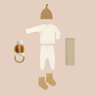 Baby clothing and accessories including a onesie, hat, socks, and rattle on a pink background