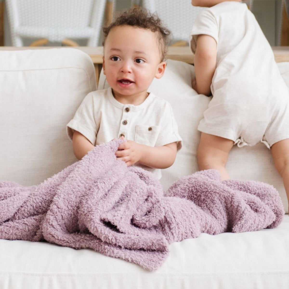 Child sitting on a couch with a pink blanket, wearing a white shirt.