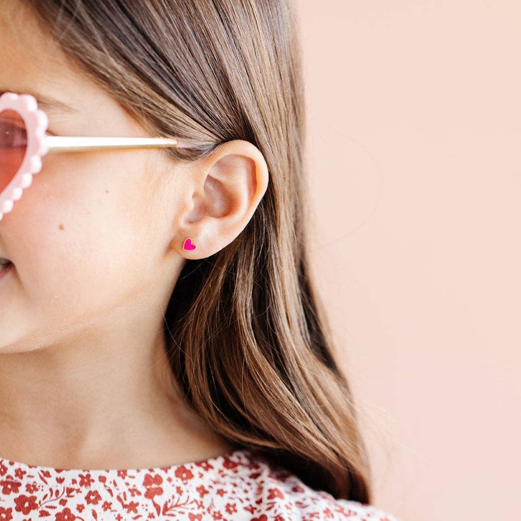 Close-up of a person wearing pink heart-shaped sunglasses and a matching earring.