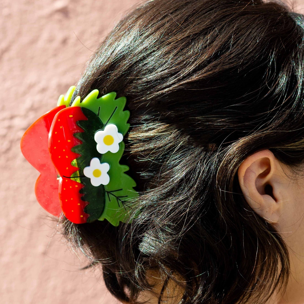 Close-up of a hair clip with red flowers and green leaves on a person's head against a pink background