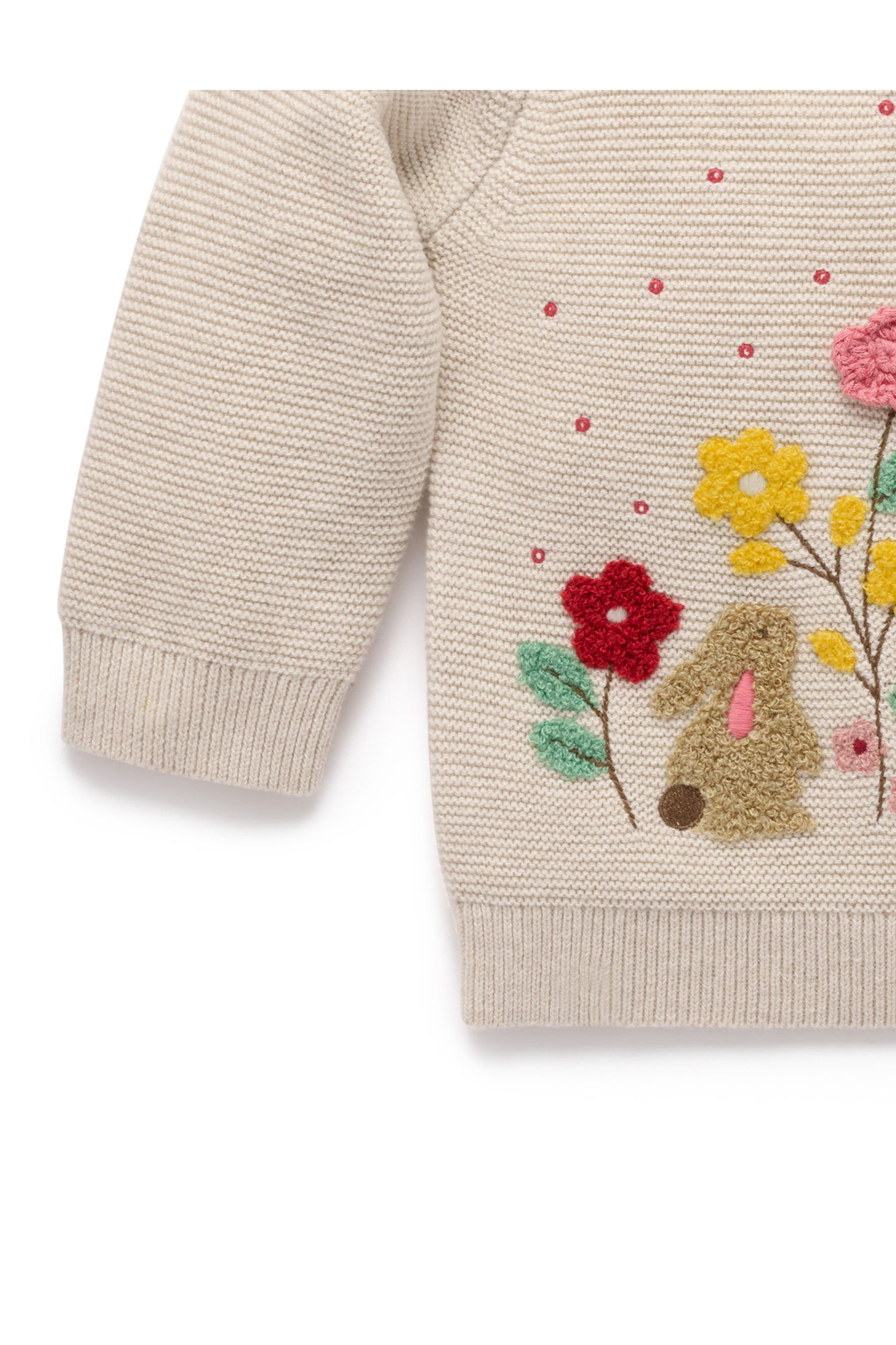 Close-up of a cream-colored knit sweater featuring a colorful embroidered bunny and wildflower design on the front.