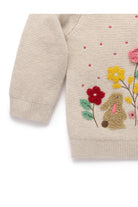 Close-up of a cream-colored knit sweater featuring a colorful embroidered bunny and wildflower design on the front.