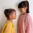 Two young girls wearing colorful hair clips and standing close to each other against a plain background.