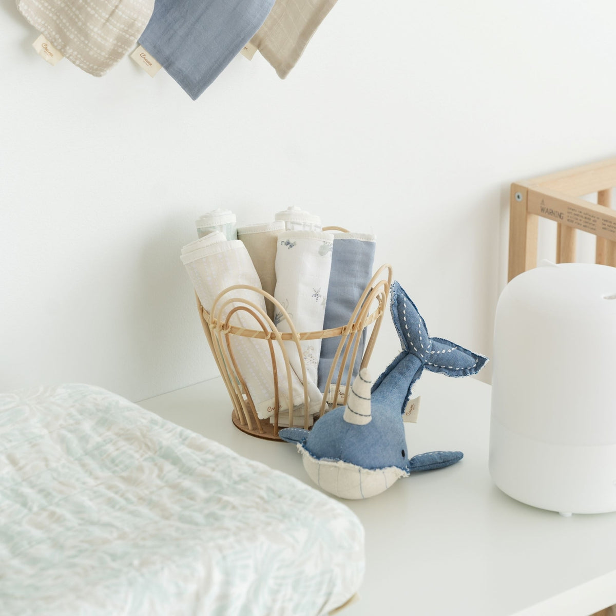 Nursery with baby clothes, a plush toy, and a basket on a white surface.