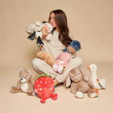 Woman holding a collection of plush toys against a beige background