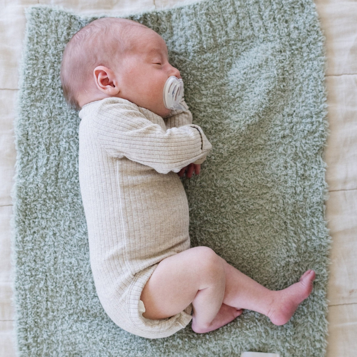 Newborn baby lying on a textured green blanket with a pacifier.