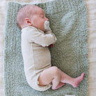 Newborn baby lying on a textured green blanket with a pacifier.