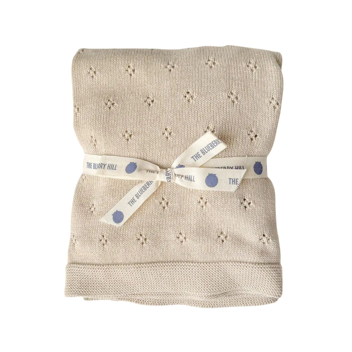 Folded beige blanket with a white ribbon and 'The Blueberry Hill' label on a white background