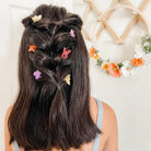 Back view of a person with braided hair adorned with colorful hair clips against a light background.