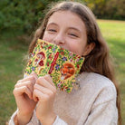 Young girl holding a colorful book with nature-themed illustrations in an outdoor setting.