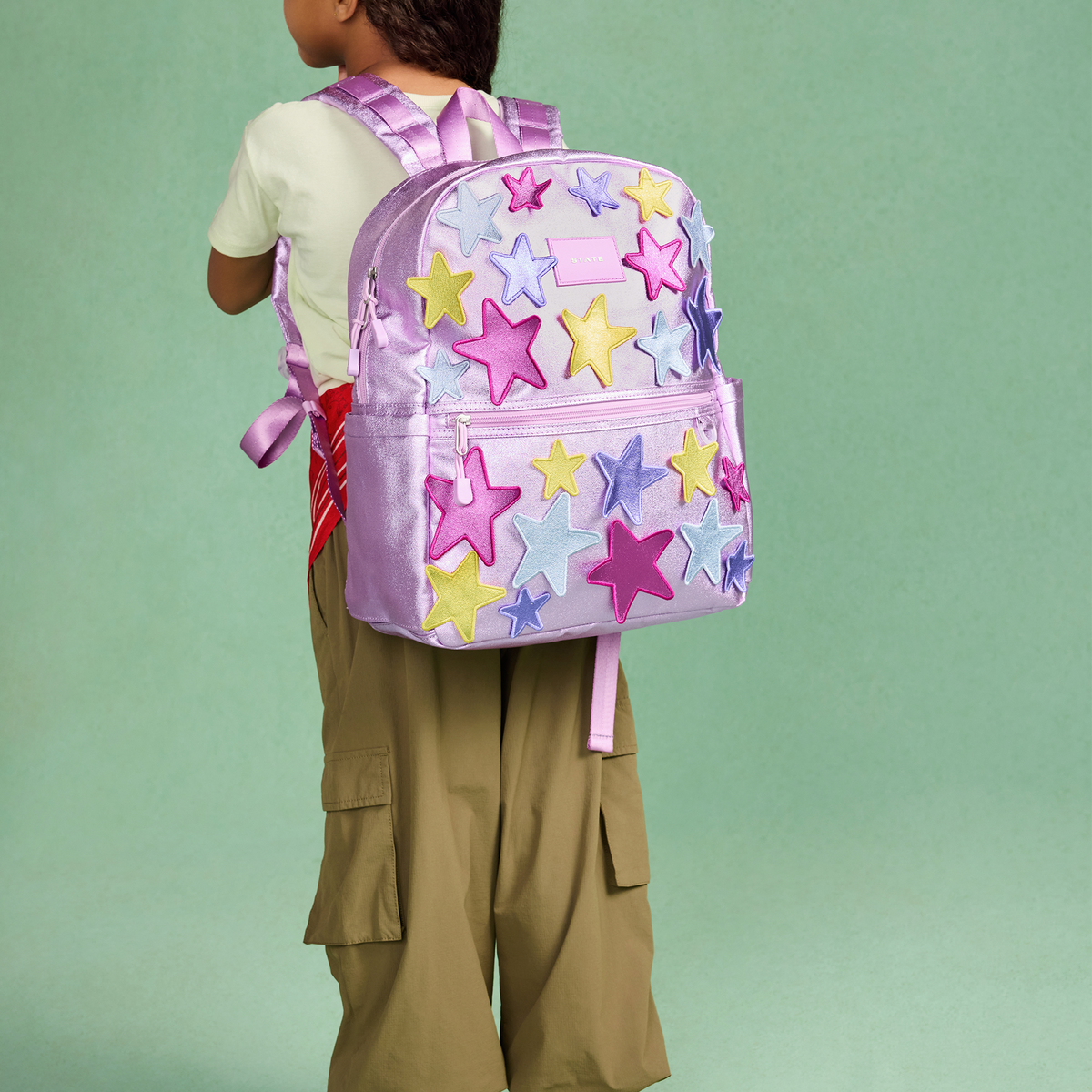 Child wearing a pink backpack with colorful star patterns on a green background