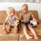 Two young children sitting on a couch with toys, one holding a toy lion and the other a toy cow.